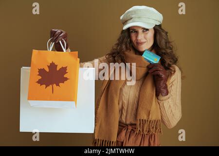 Bonjour septembre. Femme au foyer pensive et tendance de 40 ans dans un chandail avec des gants en cuir et un sac à provisions en papier isolé sur fond de bronze. Banque D'Images