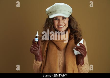 Bonjour novembre. Portrait d'une jeune femme heureuse en foulard avec mouchoirs en papier, squeiche nasale et gants en cuir sur fond marron. Banque D'Images