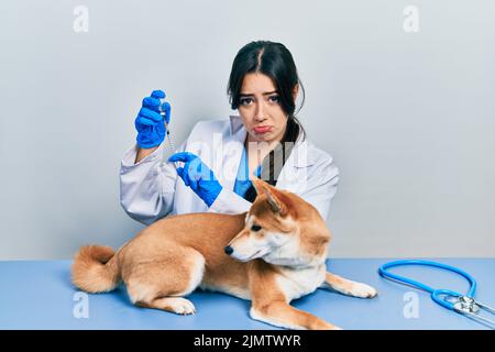 Belle femme vétérinaire hispanique mettant le vaccin à chien chiot déprimé et s'inquiéter de la détresse, pleurant en colère et peur. Expression triste. Banque D'Images