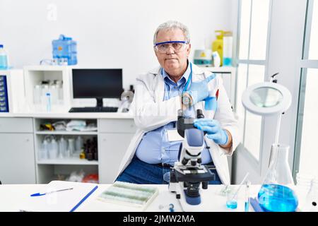 Homme caucasien senior travaillant au laboratoire scientifique pointant du doigt vers le côté montrant la publicité, sérieux et calme visage Banque D'Images