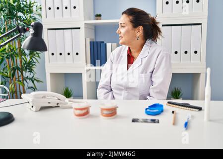Femme de dentiste mature hispanique travaillant à la clinique regardant à côté, détendez-vous profil poser avec le visage naturel avec le sourire confiant. Banque D'Images