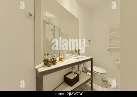 Salle de bains avec lavabo en résine design, miroir fin avec cadre en métal brossé, grand miroir sans cadre au mur et pantoufles blanches au sol Banque D'Images