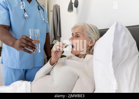 Section médiane d'un agent de santé masculin donnant un verre d'eau à une femme âgée de race blanche couché sur le lit Banque D'Images