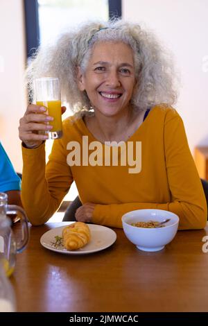 Portrait d'une femme de race blanche ayant un croissant, de l'avoine et du jus au petit déjeuner à la table du dîner Banque D'Images