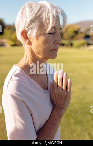 Femme asiatique âgée avec les yeux fermés méditant en position de prière dans la cour contre ciel clair Banque D'Images