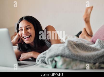 L'Internet ne manque pas de rire. Une jeune femme utilisant un ordinateur portable tout en se relaxant au lit à la maison. Banque D'Images