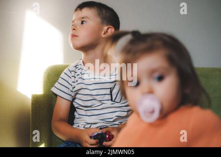 Deux enfants attendent à la maison sur le canapé pour que leurs parents reviennent du travail. Bonne famille, enfance. Fille souriante. Une enfance insouciante. Banque D'Images