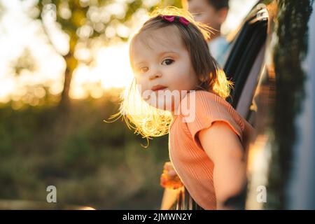 Portrait d'une petite fille qui colle la tête par la fenêtre de la voiture pour admirer la nature. Vacances d'été. Bonne famille, enfance. Banque D'Images