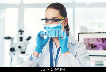 Une jeune scientifique méconnaissable qui pose un masque facial de protection à l'intérieur d'un laboratoire pendant la journée. Banque D'Images