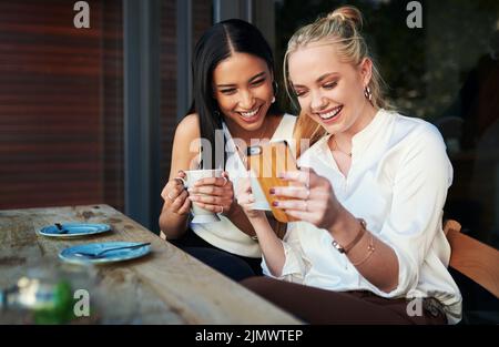 Je leur laisse une grande critique sur leur site web. Deux jeunes femmes regardant quelque chose sur un téléphone portable tout en étant assis dans un café. Banque D'Images