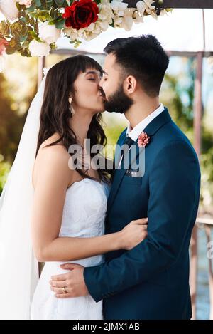 Un baiser est une autre façon de communiquer l'amour avec vos lèvres. Un jeune couple affectueux et jeune, qui embrasse tout en se tenant debout à l'extérieur le jour de leur mariage. Banque D'Images