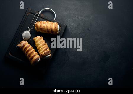 Tubes cuits remplis de crème blanche aux œufs fouettés sur un plan de cuisine en bois noir, vue du dessus Banque D'Images