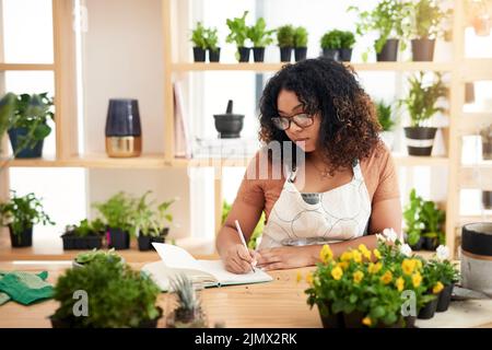 Elle prend la botanique au sérieux. Une jeune femme botaniste attrayante prenant des notes tout en travaillant dans son fleuriste. Banque D'Images