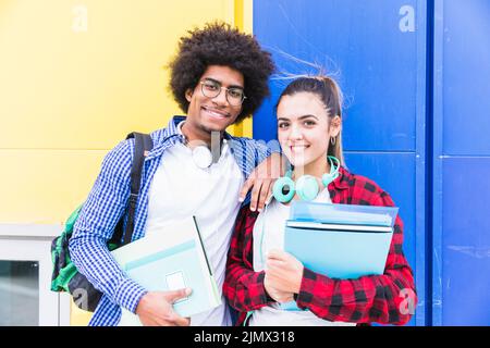 Jeune couple tenant des livres main debout contre le mur bleu jaune Banque D'Images