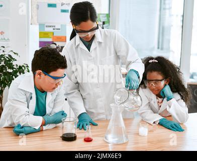 Regardez ce qui se passe quand nous faisons cela... un adorable petit garçon et une fille menant une expérience scientifique avec leur professeur à l'école. Banque D'Images