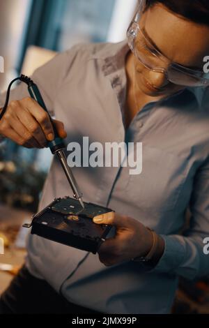 Les disques durs sont beaucoup plus durables que vous ne le pensez. Une jeune technicienne informatique attirante répare un disque dur dans son atelier. Banque D'Images