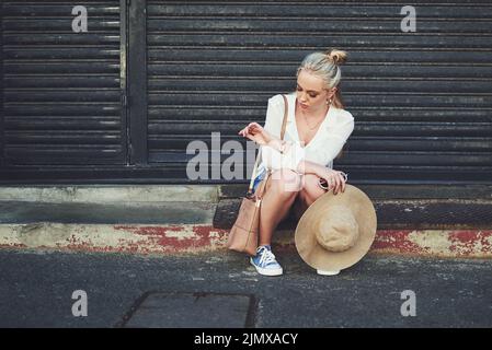 Je ne peux pas croire que je suis toujours en attente ici. Prise de vue en longueur d'une jeune femme contrariée qui vérifie l'heure sur sa montre-bracelet tout en étant assise à l'extérieur. Banque D'Images