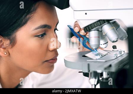 Il est temps de faire une enquête sérieuse. Gros plan d'une jeune scientifique attrayante plaçant une lame microscopique sous le microscope pendant Banque D'Images