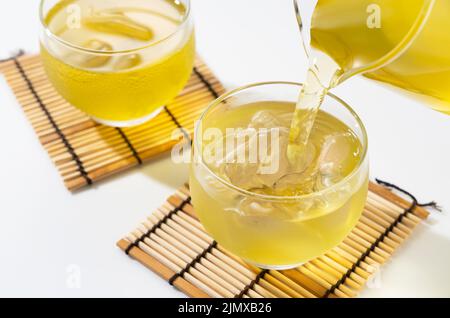 Verser le thé vert dans une théière en verre remplie de glace. Boisson japonaise d'été. Banque D'Images