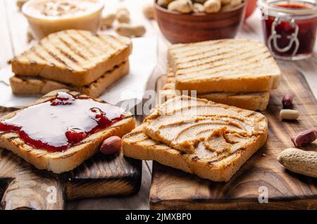 Vue à bas angle sur le beurre d'arachide et les sandwichs de confiture à bord de la planche à découper avec toasts de côté. Concept de saine alimentation Banque D'Images