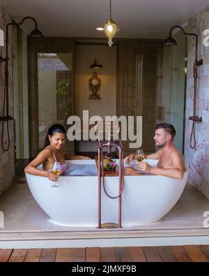 Baignoire romantique avec pétales de rose, vacances de luxe dans le jacuzzi, couple hommes et femme dans la salle de bain Banque D'Images