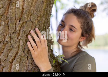 Une jeune femme contentée embrassant un grand arbre avec une expression blissful et ses yeux fermés dans un concept de sauver la forêt, arrêter Banque D'Images