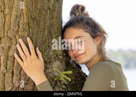 Une jeune femme contentée embrassant un grand arbre avec une expression blissful et ses yeux fermés dans un concept de sauver la forêt, arrêter Banque D'Images