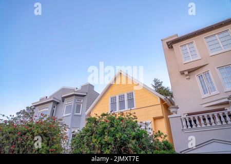 Maison à pignon jaune au milieu de deux maisons avec mur extérieur en béton peint. Façade de trois maisons à San Francisco, Californie avec différents Banque D'Images