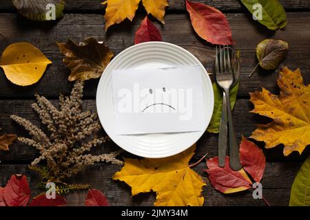 triste smiley est tiré sur papier se trouve sur une plaque blanche sur une table en bois dans les feuilles jaunes d'automne, tristesse tristesse tristesse depremia, crise n'a rien à manger Banque D'Images