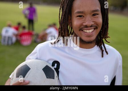 Portrait en gros plan d'un joueur biracial masculin avec des dreadlocks tenant le ballon de football dans l'aire de jeux Banque D'Images