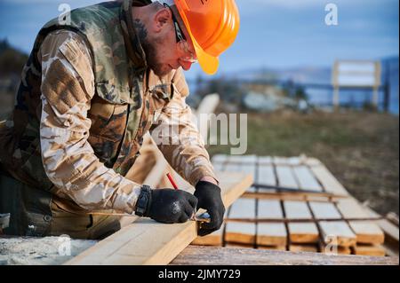 Homme ouvrier bâtiment maison en bois cadre. Menuisier mesurant des planches en bois et faisant des marques avec un crayon. Concept de menuiserie. Banque D'Images