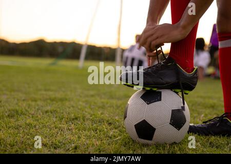 Coupe basse d'un homme caucasien portant des chaussettes rouges avec une jambe sur le ballon de football nouant le cordonnet Banque D'Images