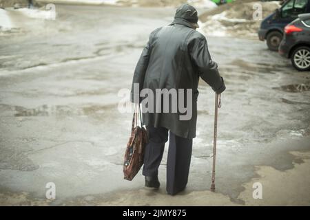 Une femme avec un bâton de pore marche dans la rue tout en marchant. Retraité en Russie. La vieille femme marche avec le sac dans sa main. Banque D'Images