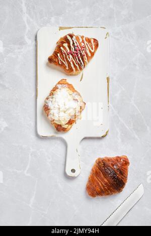 Vue de dessus d'un assortiment de croissants frais sur plateau de service blanc sur fond de marbre Banque D'Images