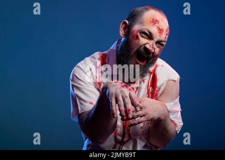 Dangereux regarder halloween zombie attaquant caméra sur fond bleu, cerveau mangeant corps effrayant avec des blessures sanglantes. Monstre effrayant et cruel avec un regard effrayant et apocalyptique. Banque D'Images