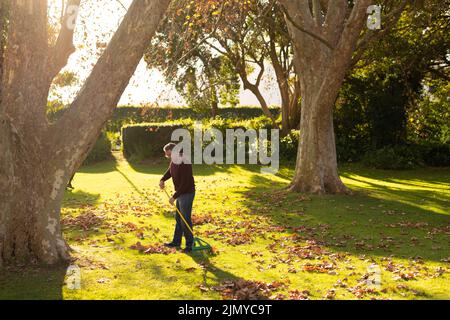 Image d'un homme âgé caucasien heureux qui balaie les feuilles dans le jardin Banque D'Images