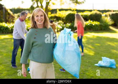 Image d'une femme de race blanche heureuse avec des sacs de déchets dans le jardin Banque D'Images