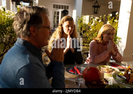 Image de plusieurs générations de famille caucasienne priant avant le dîner en plein air Banque D'Images