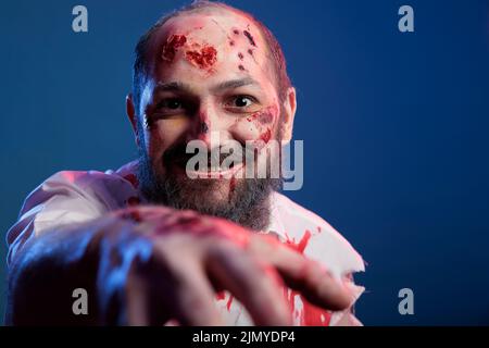 Un zombie d'halloween effrayant s'approchant de la caméra en studio, l'air effrayant et dangereux avec des cicatrices et des blessures sanglantes. Un monstre sinistre apocalyptique avec un visage effrayant et des yeux fous mangeant le cerveau. Banque D'Images