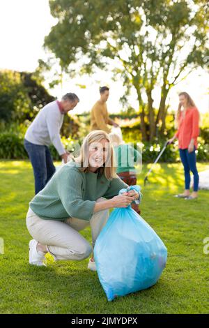 Image verticale de la bonne femme caucasienne avec des sacs de déchets dans le jardin Banque D'Images