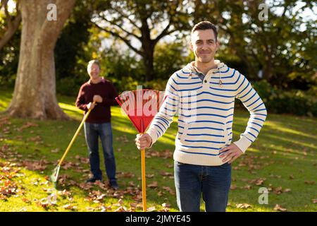 Image d'un père caucasien et d'un fils adulte qui balaie les feuilles dans le jardin Banque D'Images