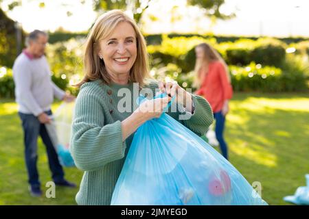 Image d'une femme de race blanche heureuse avec des sacs de déchets dans le jardin Banque D'Images