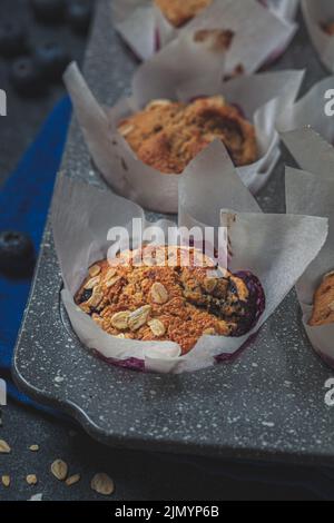 Flocons d'avoine végétaliens, bananes, muffins aux myrtilles sur fond bleu, gros plan. Dessert à base de plantes. Banque D'Images