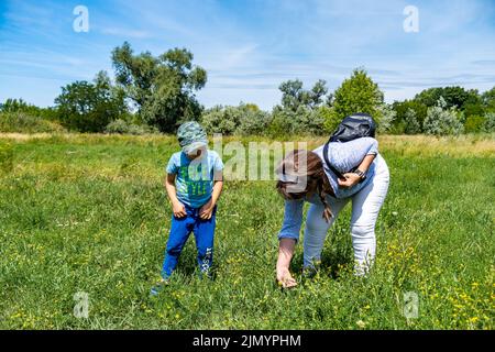 Une femme et un enfant à la recherche d'insectes dans l'herbe verte haute et les mauvaises herbes près de la rue Bernata par une journée ensoleillée Banque D'Images