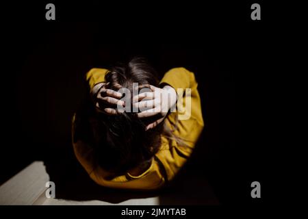 Vue de dessus d'une femme méconnaissable souffrant de dépression et pleurant à la maison, tenant la tête dans ses mains. Banque D'Images