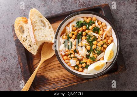 Ragoût de pois chiches avec des épinards et de la morue ou potaje de vigilia dans un bol sur le plateau en bois sur la table. Vue horizontale du dessus Banque D'Images