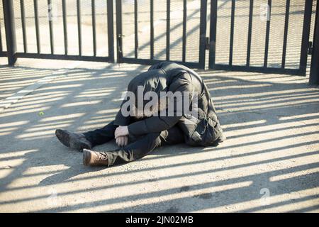 Guy est assis sur le trottoir. Homme sans abri dans la rue. Ivre est allé en bas. L'homme a tout perdu. Banque D'Images