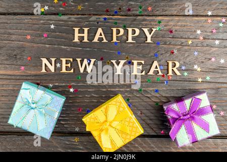 Boîtes-cadeaux multicolores avec noeuds noués. Nouvel an présente sur une table en bois avec des étoiles confetti éparpillées. Texte Bonne Année. Carte de vœux de fête. F Banque D'Images