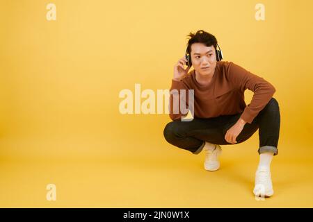 Jeune homme dans des clothers décontractés à l'écoute de la musique dans des écouteurs Banque D'Images