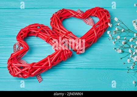 Deux coeurs en osier rouge sur un bureau en bois bleu. Petites fleurs blanches. Banque D'Images